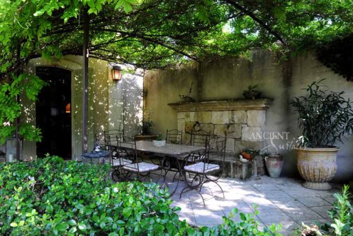Outdoor Courtyard with heavy foliage, a wall fountain and an outdoor dining table by Ancient Surfaces. 