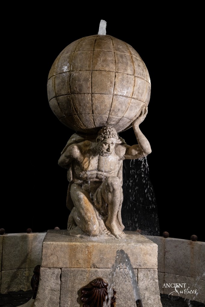 Vintage limestone fountain reclaimed by Ancient Surfaces, featuring a sculpture of a man holding a sphere over his head, with water gracefully cascading down.