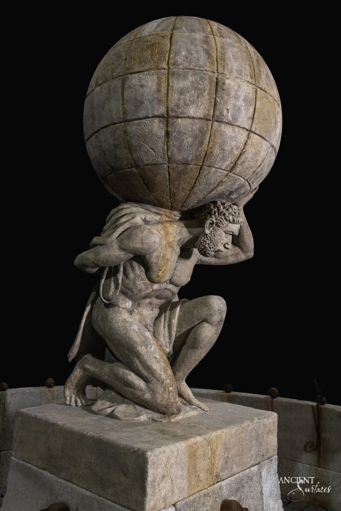 Vintage limestone fountain reclaimed by Ancient Surfaces, featuring a statue of a man holding a sphere over his head, reminiscent of classic Greek sculpture.