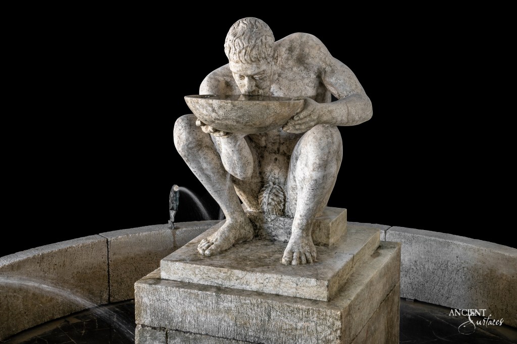 Antique limestone fountain by Ancient Surfaces, featuring a statue of a man drinking water from a platter, a nod to the timeless charm of classical sculpture.