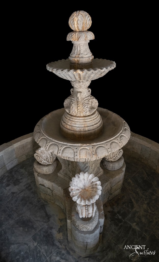Ancient Greek-style limestone fountain by Ancient Surfaces, adorned with intricate shell carvings and other classical motifs, showcasing the timeless beauty of historical artistry.